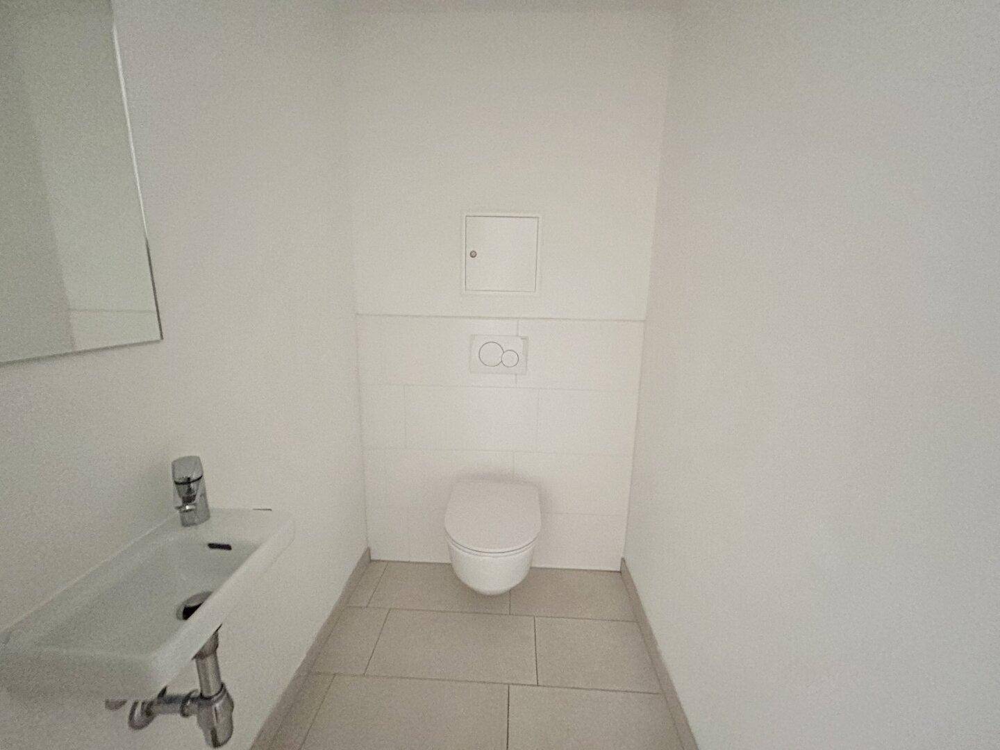 Modernes Gäste-WC mit wandhängender Toilette, kleinem Waschbecken und hellen Fliesen.