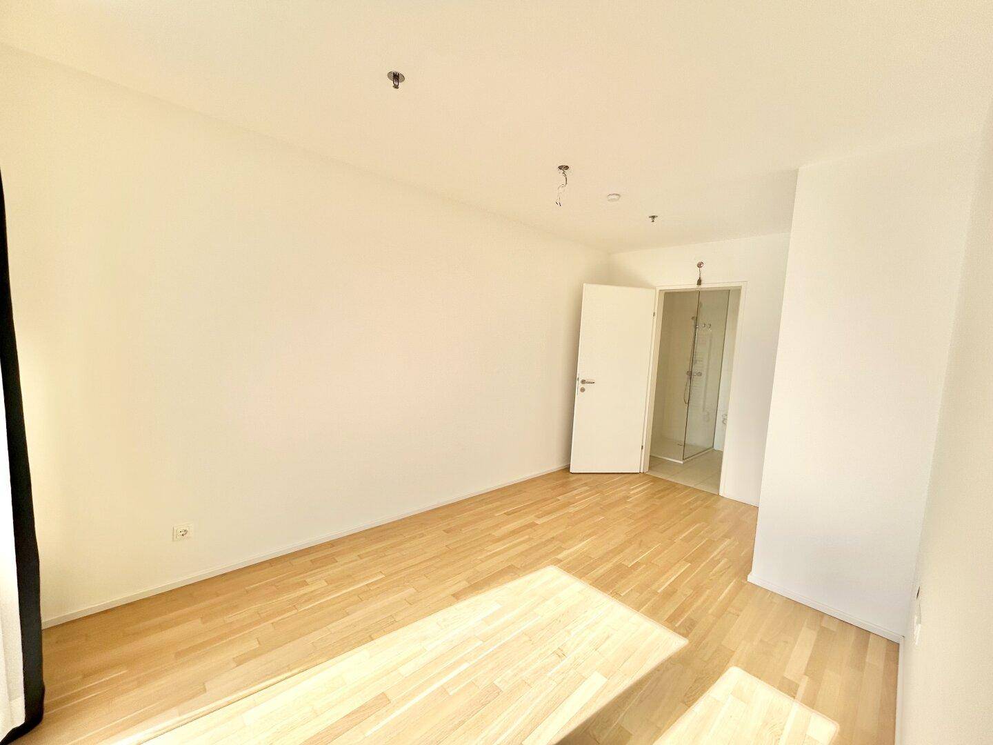 Helles Schlafzimmer mit Holzboden und direktem Zugang zu einem modernen Badezimmer.