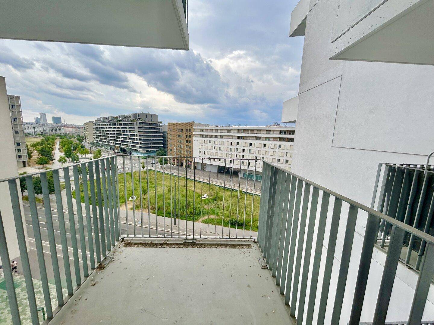 Balkon mit Blick auf die Stadt, eine Grünfläche und umliegende Gebäude.