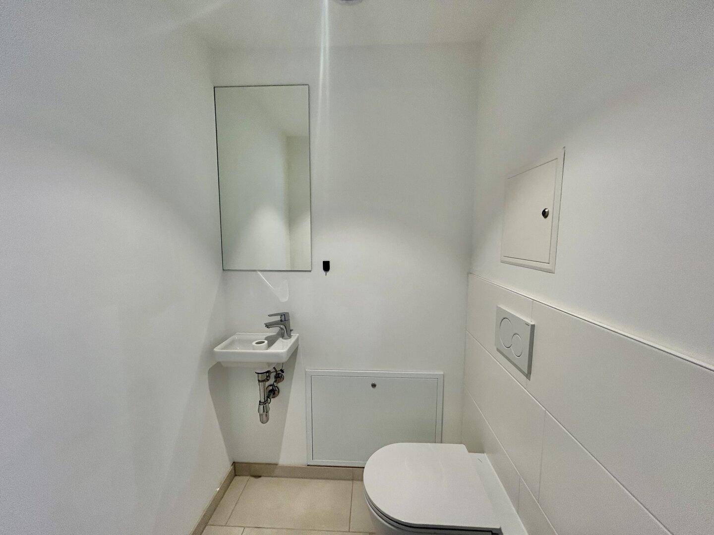 Modernes Gäste-WC mit Wand-WC, kleinem Waschbecken und hellem Fliesenboden.