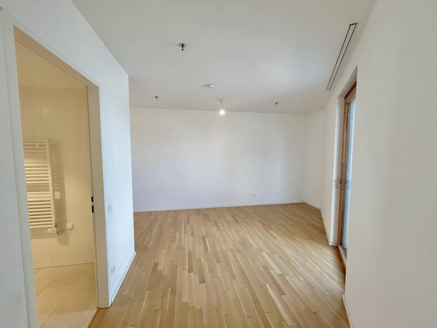 Heller Wohnraum mit Parkettboden und großen Fenstern, die viel Tageslicht hereinlassen.