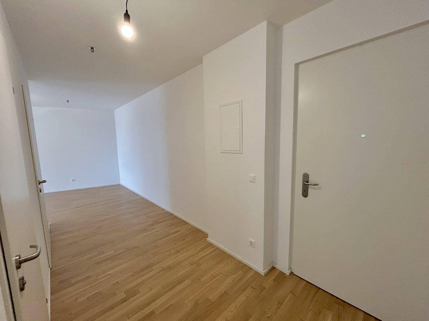 Langer, heller Flur mit Holzboden und weiß gestrichenen Wänden, der den Eingangsbereich verbindet.