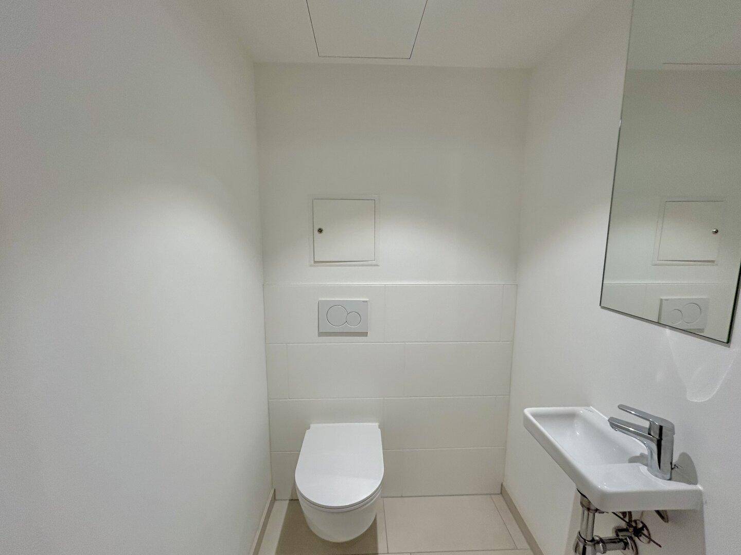Modernes Gäste-WC mit wandhängendem WC, kleinem Waschbecken und hellen Fliesen.