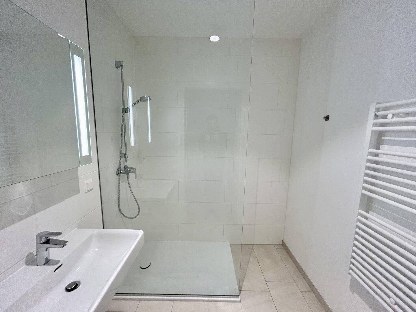 Modernes Badezimmer mit ebenerdiger Dusche, Einzelwaschbecken und beheiztem Handtuchhalter.