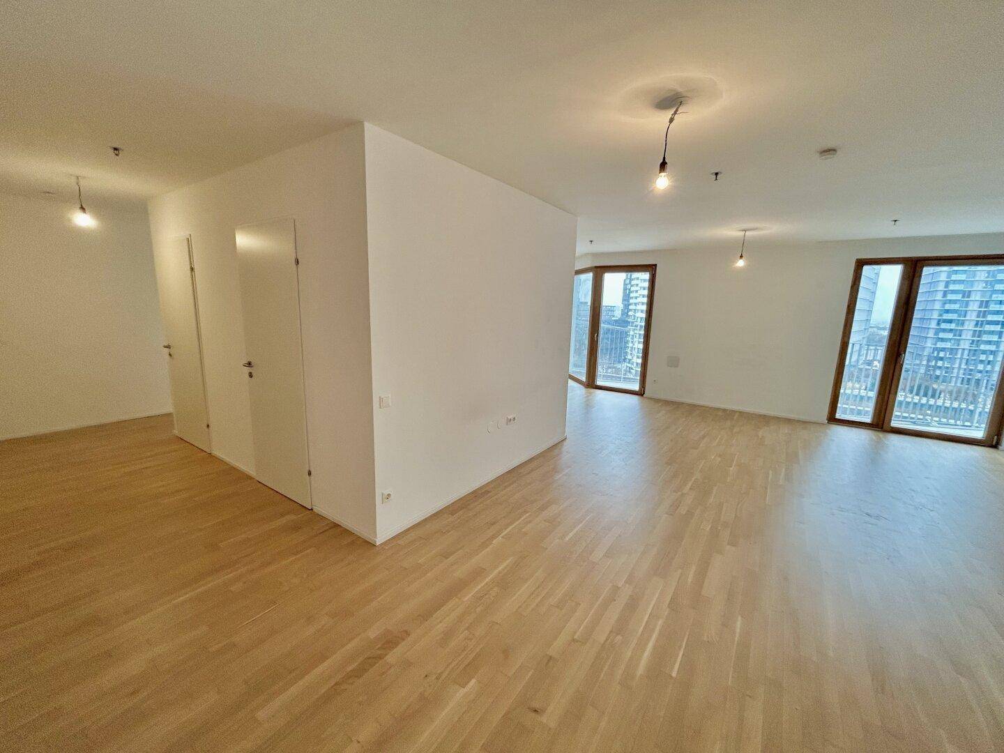 Geräumiger Wohnbereich mit großen Fenstern, Parkettboden und viel Tageslicht.