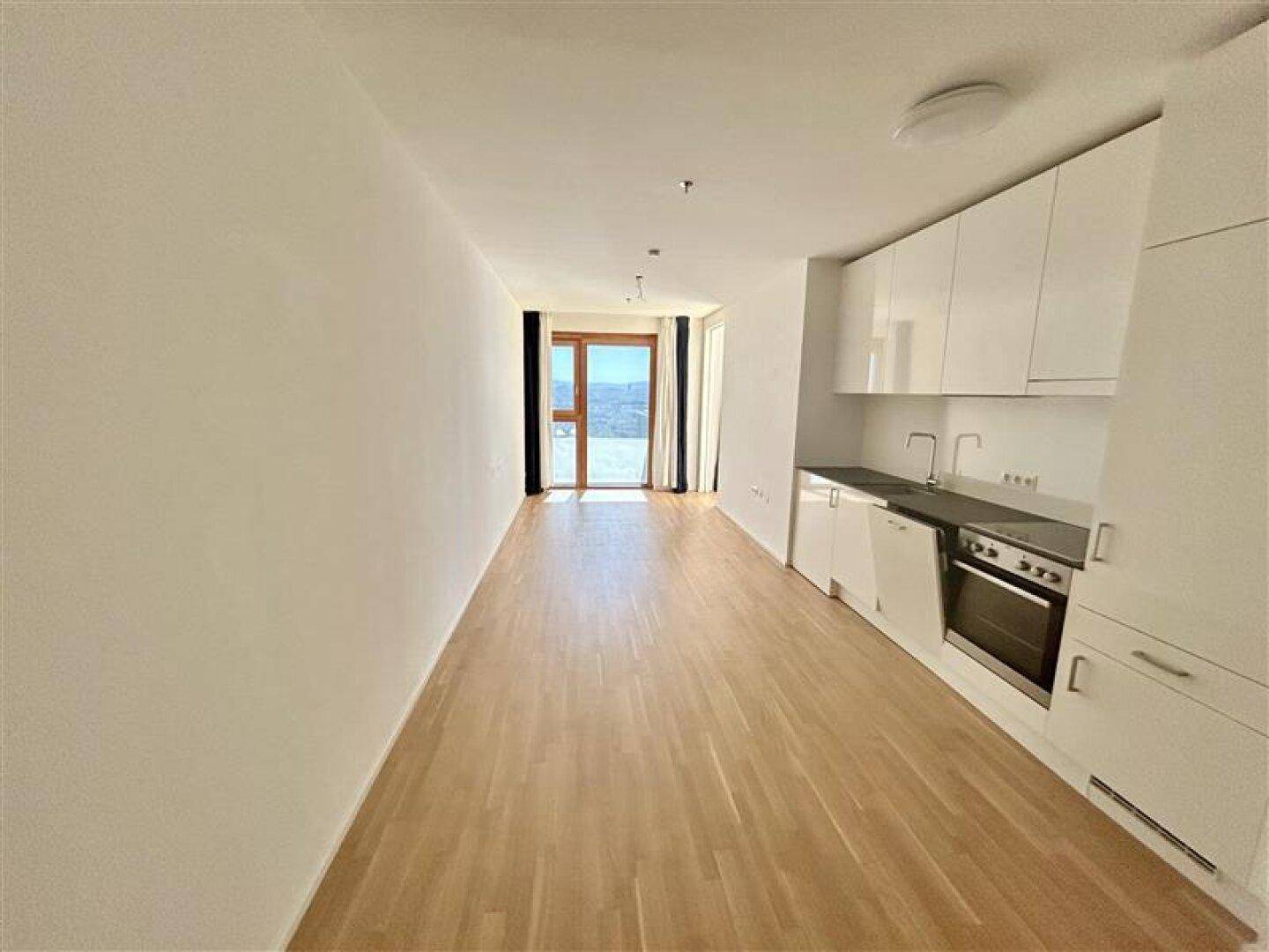 Lichtdurchfluteter Wohnbereich mit moderner Küchenzeile und Zugang zu einem Balkon.