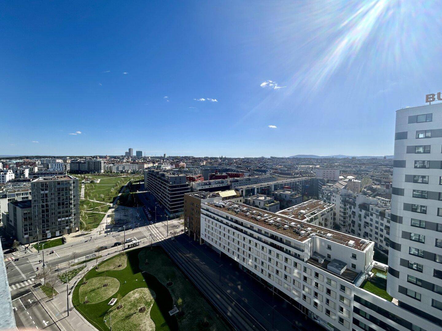 Panoramablick über eine moderne Stadtlandschaft mit neuen Gebäuden und Grünflächen unter blauem Himmel.