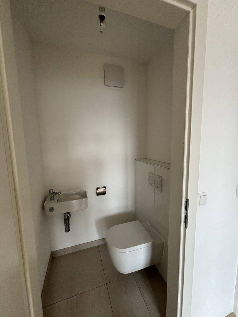 Modernes Gäste-WC mit wandhängender Toilette, kleinem Waschbecken und Fliesenboden.