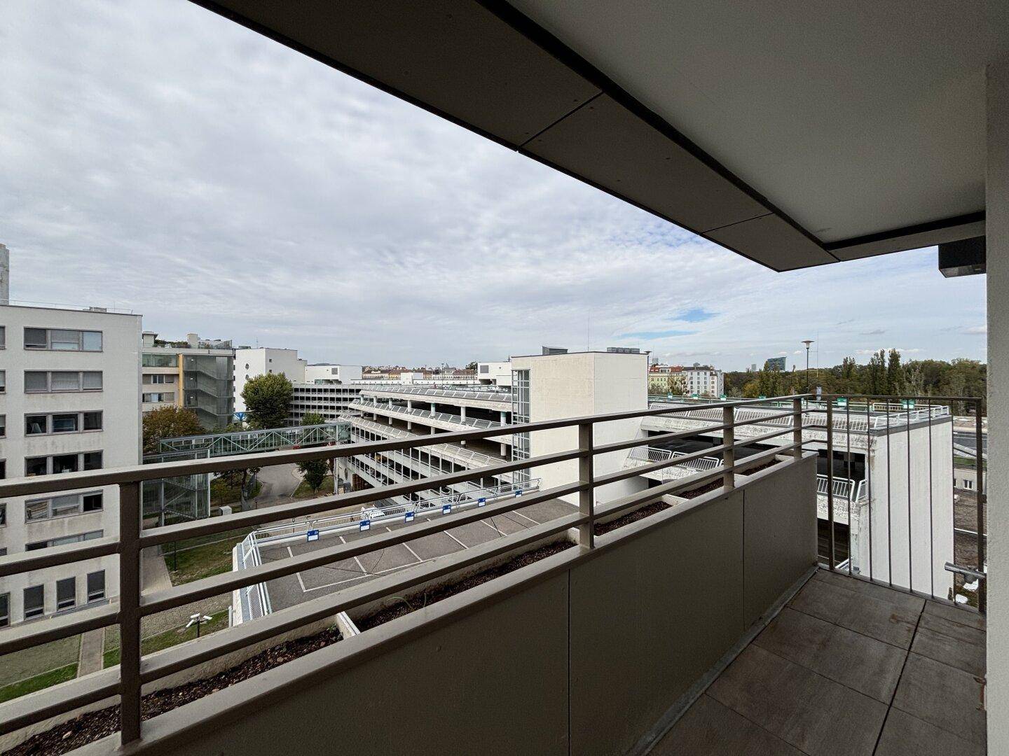 Ausblick von einem Balkon auf eine Parkgarage und umliegende Wohngebäude.