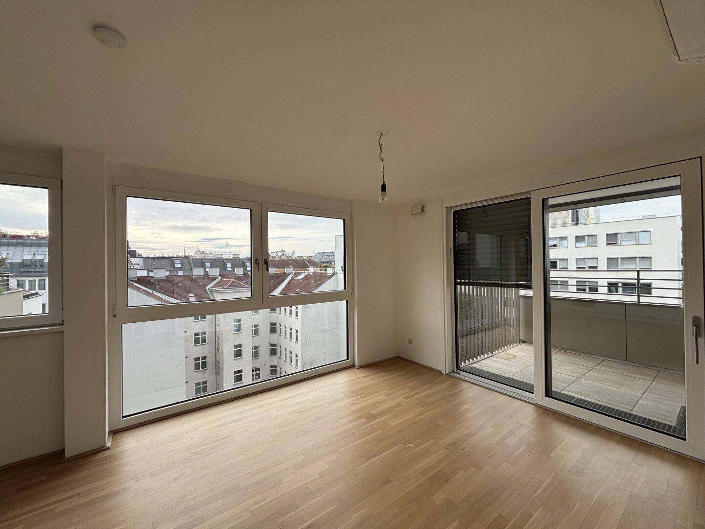 Helles Wohnzimmer mit Parkettboden, großen Fenstern und Zugang zu einem Balkon.