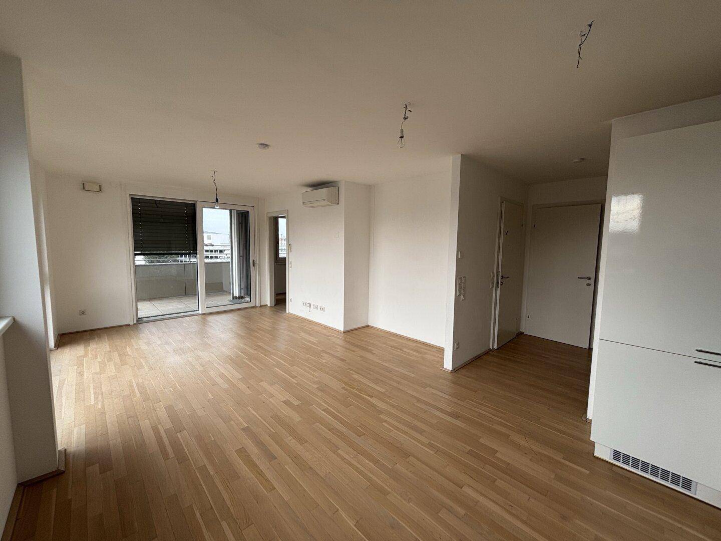 Geräumiges Wohnzimmer mit Parkettboden, Klimaanlage und Schiebetür zum Balkon.