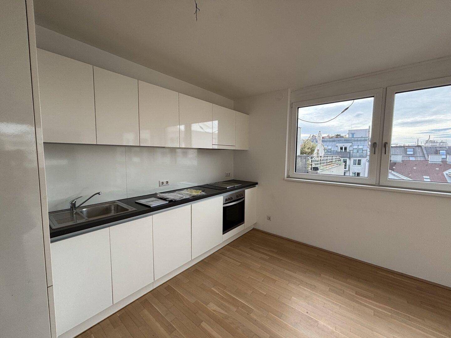 Moderne Einbauküche mit weißen Schränken, dunkler Arbeitsplatte und Fensterblick.
