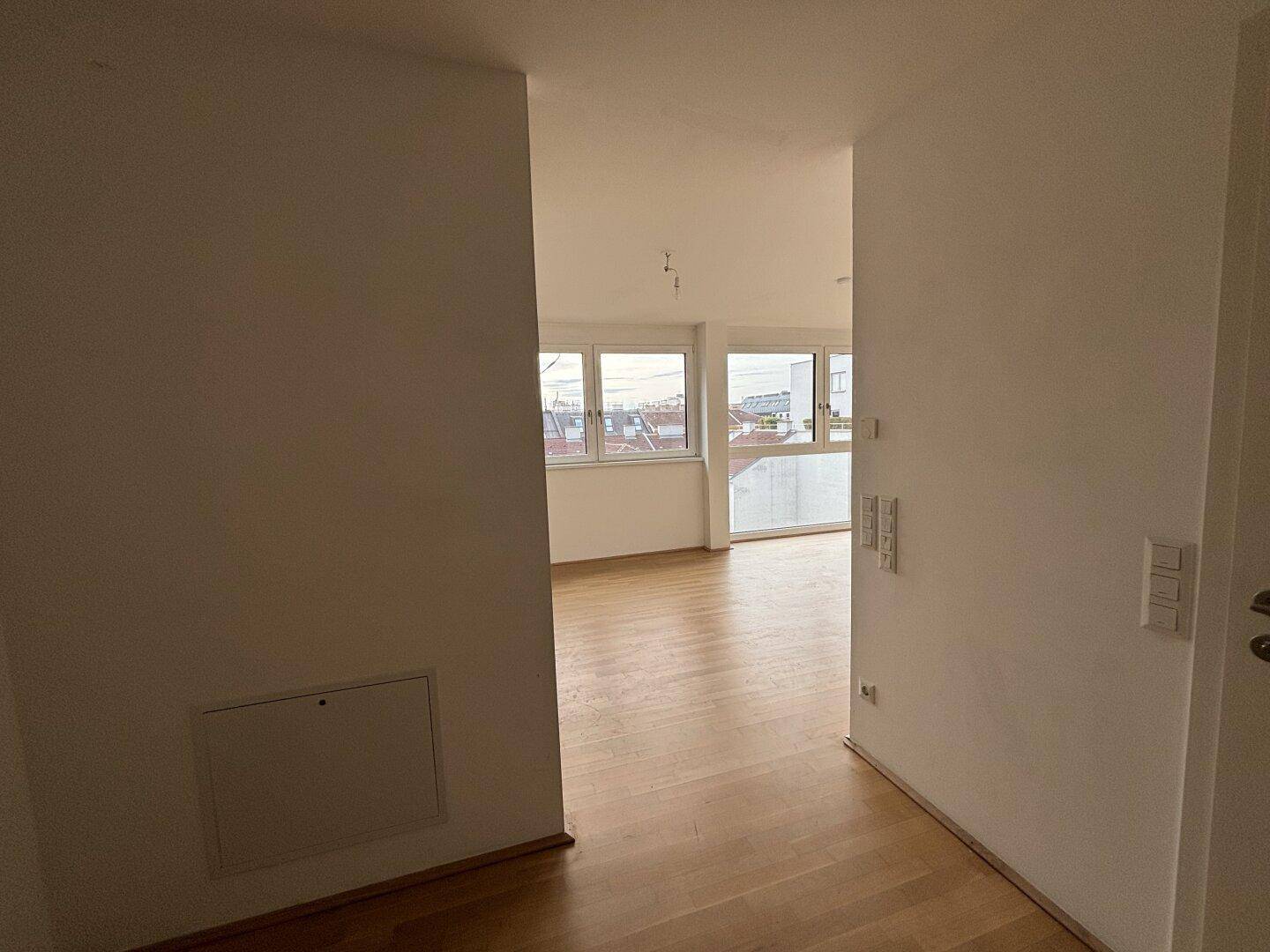 Blick vom Flur in einen offenen Wohnbereich mit großen Fenstern und Parkettboden.