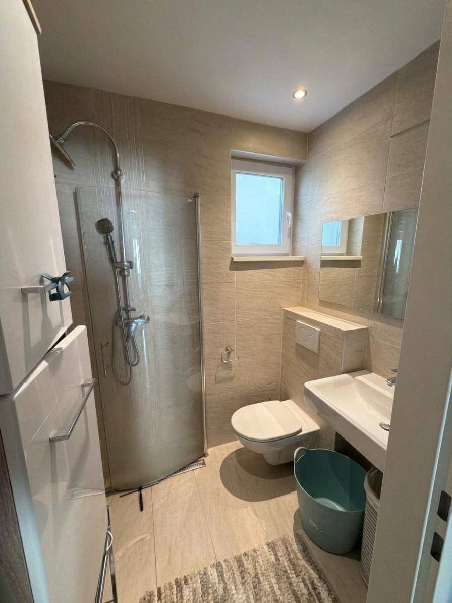 Modernes Badezimmer mit Dusche, WC, Waschbecken und einem Fenster für Tageslicht.