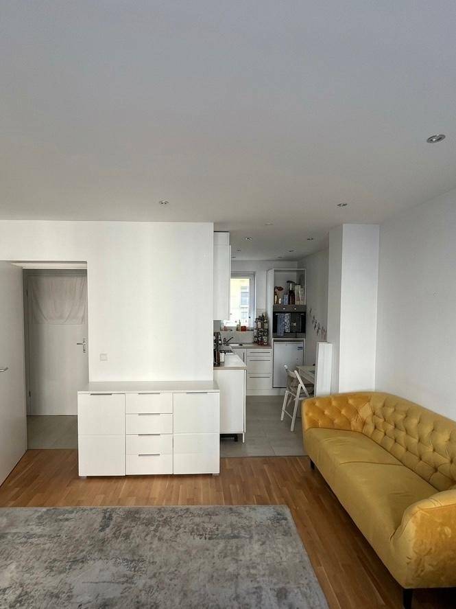 Offener Wohnbereich mit gelbem Sofa, weißem Sideboard und Blick auf die Küchenzeile.