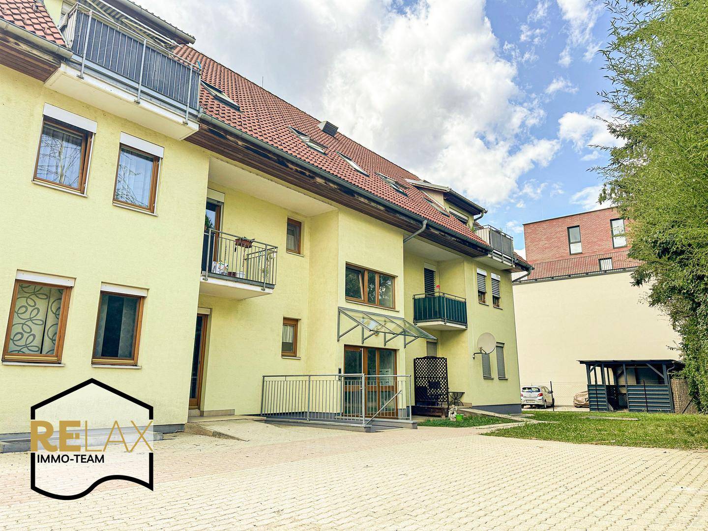 Ansicht des Wohngebäudes von außen mit Balkonen und gepflastertem Vorplatz.