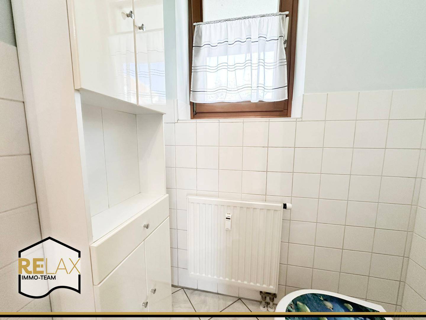 Separates WC mit weißen Fliesen, Fenster und praktischem Hochschrank.