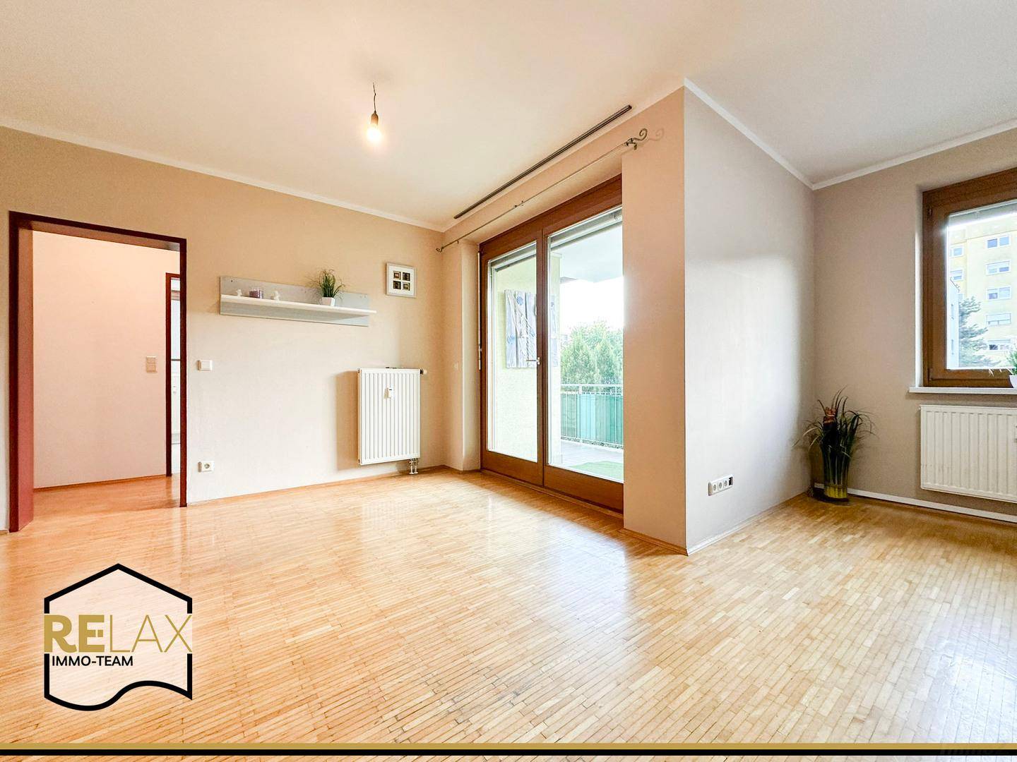 Helles Wohnzimmer mit Holzparkett, großem Fenster und Zugang zu einem Balkon.