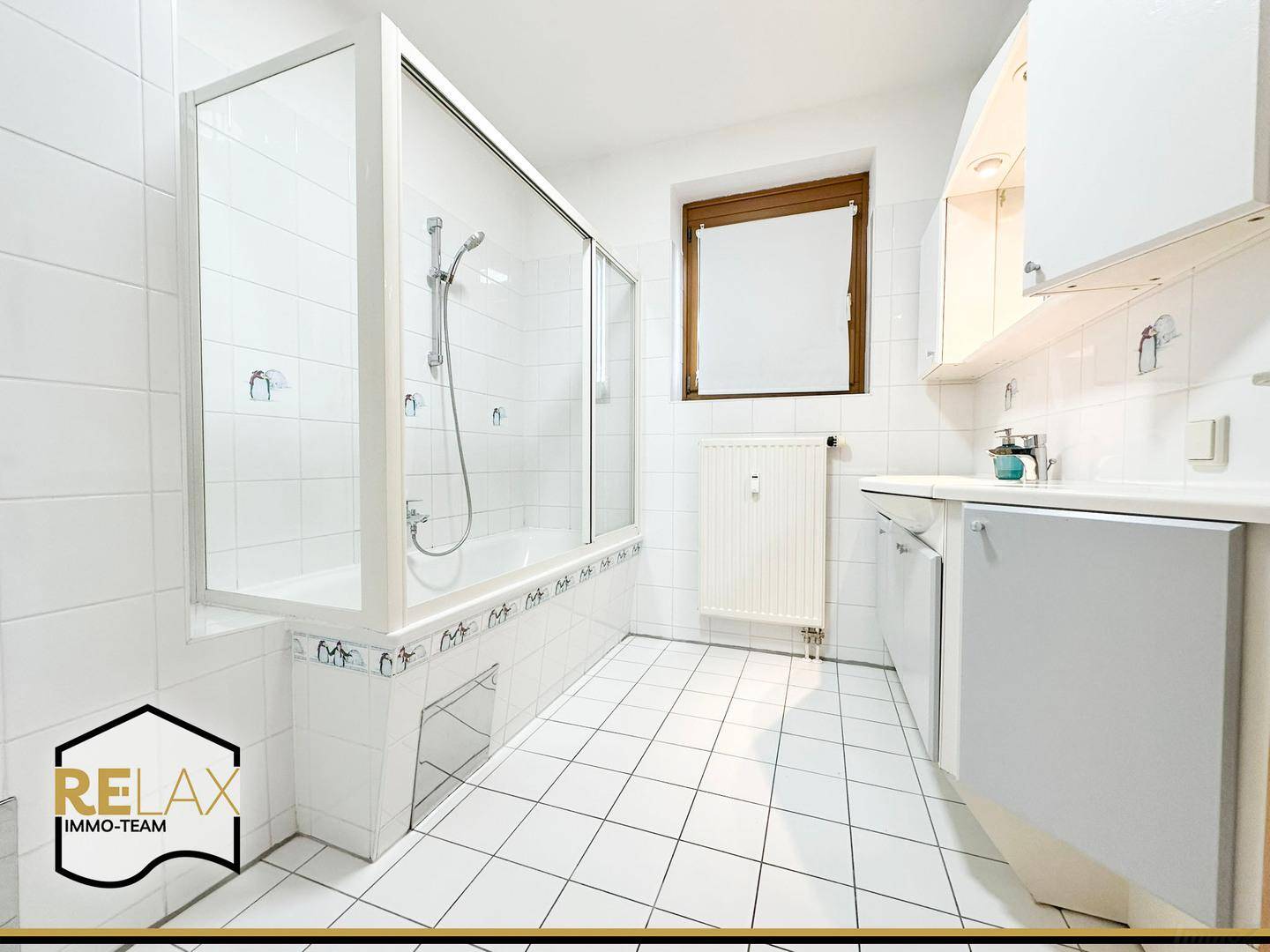 Helles Badezimmer mit weißen Fliesen, Badewanne mit Duschwand und Fenster.