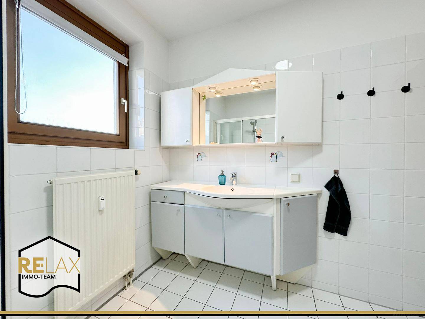 Helles Badezimmer mit Waschbecken, Spiegelschrank, weißen Fliesen und Fenster.