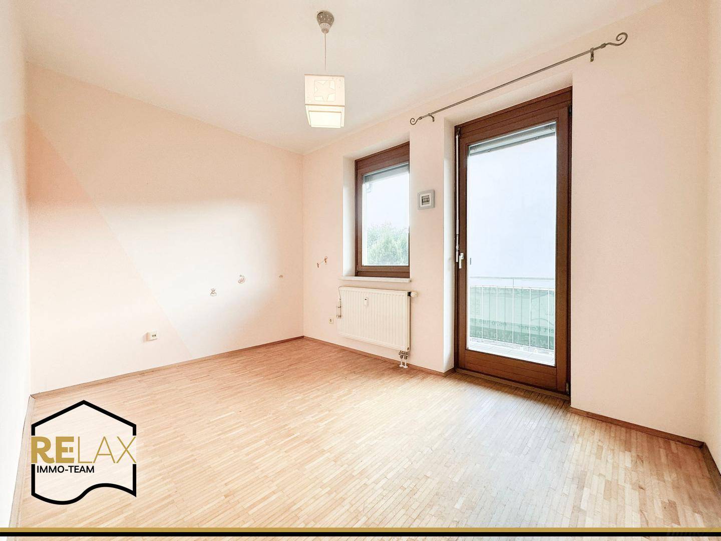 Leeres Zimmer mit Holzparkett, Fenster und direktem Zugang zu einem Balkon.