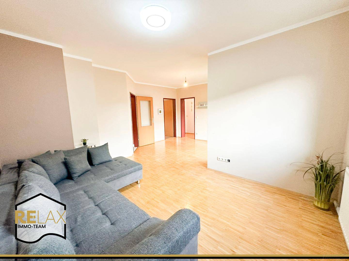Geräumiges Wohnzimmer mit modernem Ecksofa und hellem Holzparkettboden.