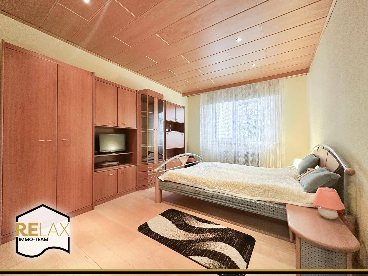 Schlafzimmer mit Holzmöbeln, Doppelbett und einem großen Fenster für viel Licht.