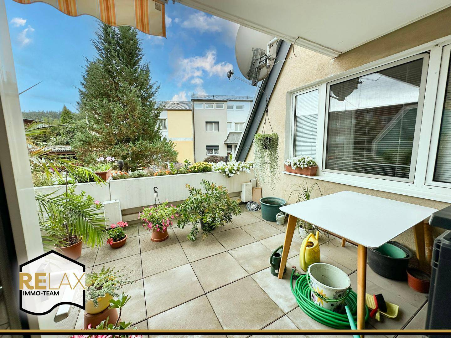 Große Terrasse mit Pflanzen, einem Tisch und Blick auf die Nachbarschaft.