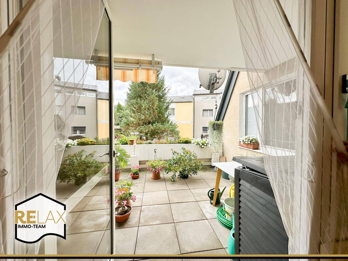 Blick vom Innenraum auf die große, begrünte Terrasse mit Markise und Sitzbereich.