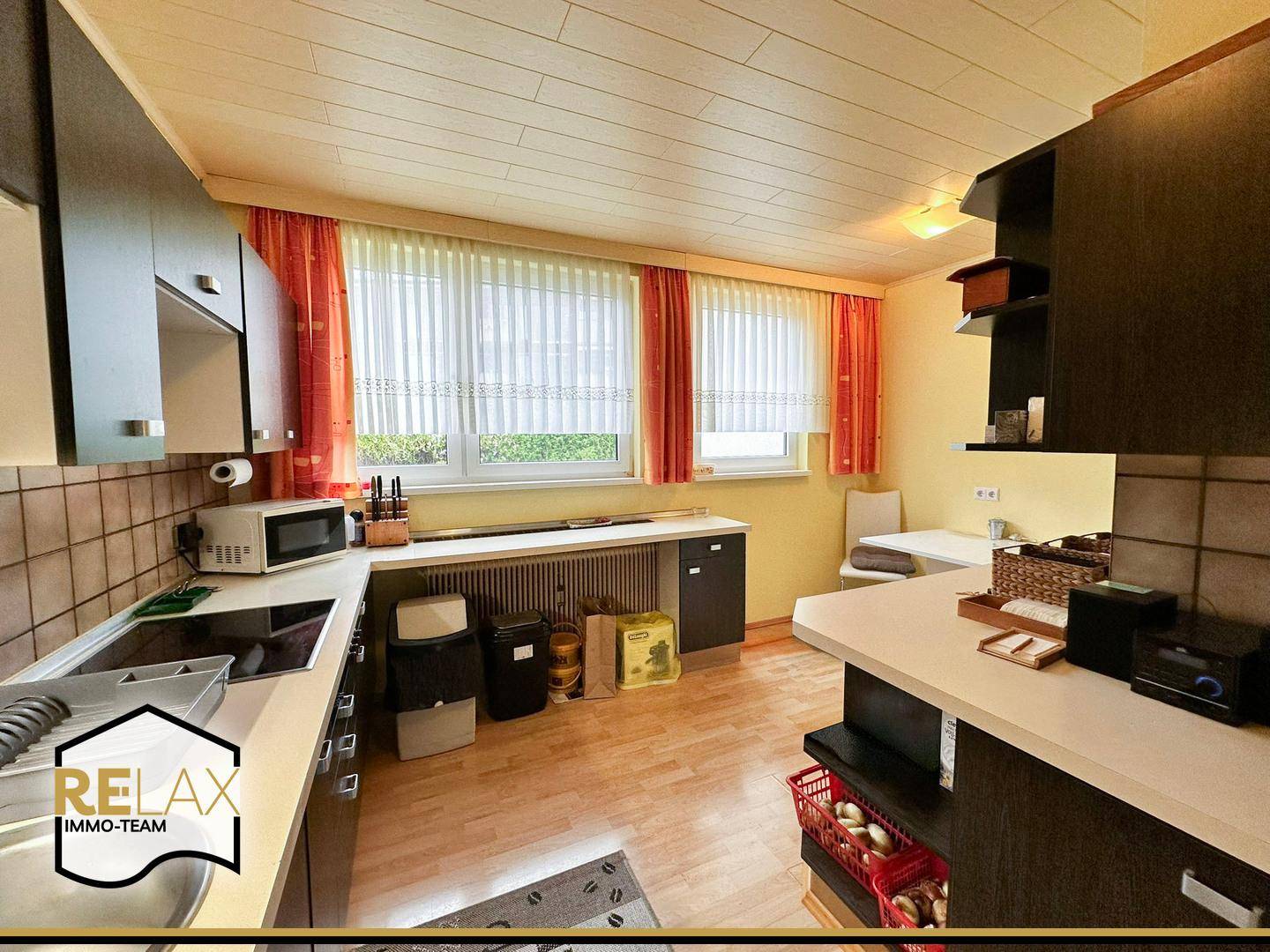 Funktionale Küche mit dunklen Schränken, Arbeitsflächen und einem Essbereich am Fenster.