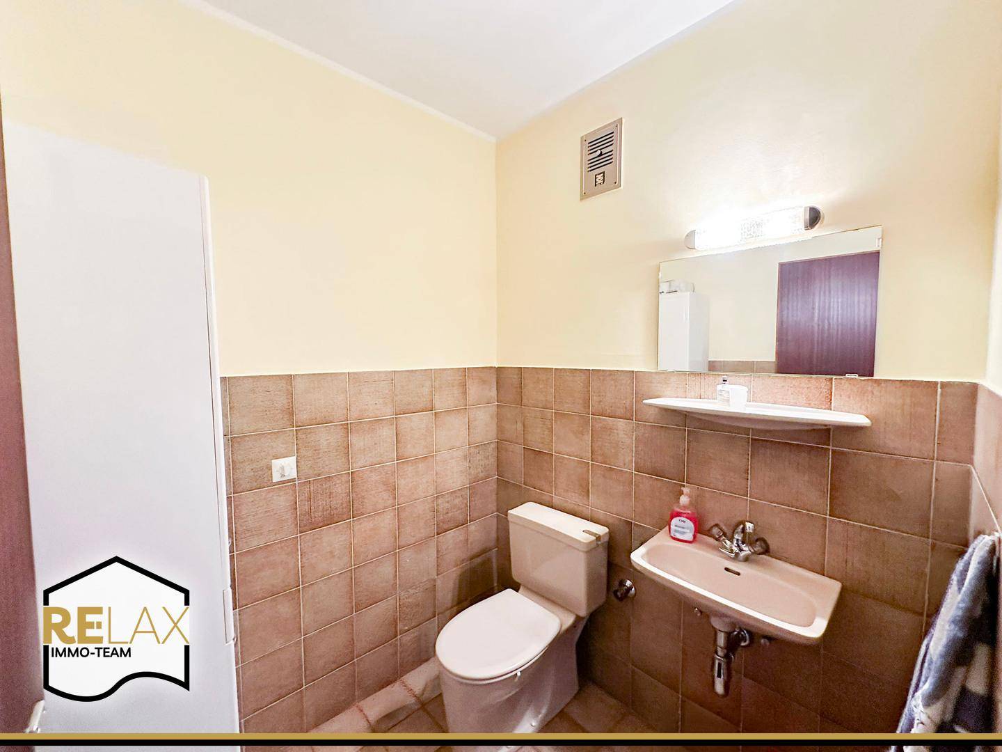 Kleines Gäste-WC mit beigefarbenen Fliesen, Toilette und Waschbecken.