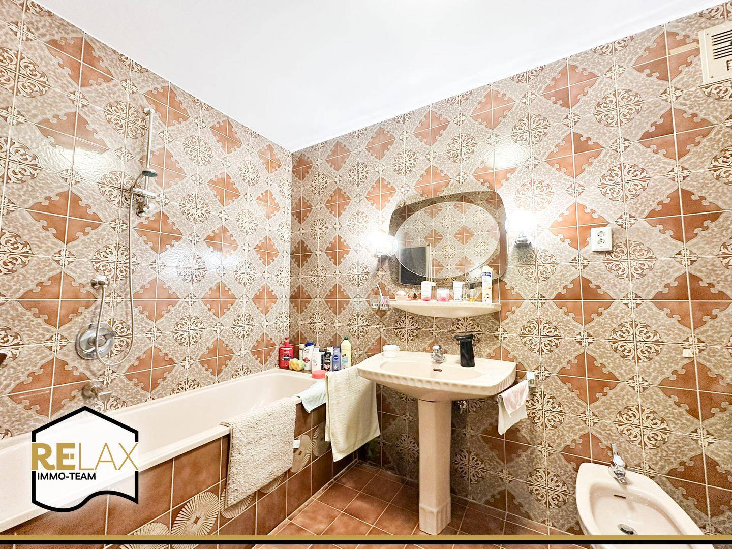 Badezimmer mit Badewanne, Waschbecken, Bidet und gemusterten Wandfliesen.