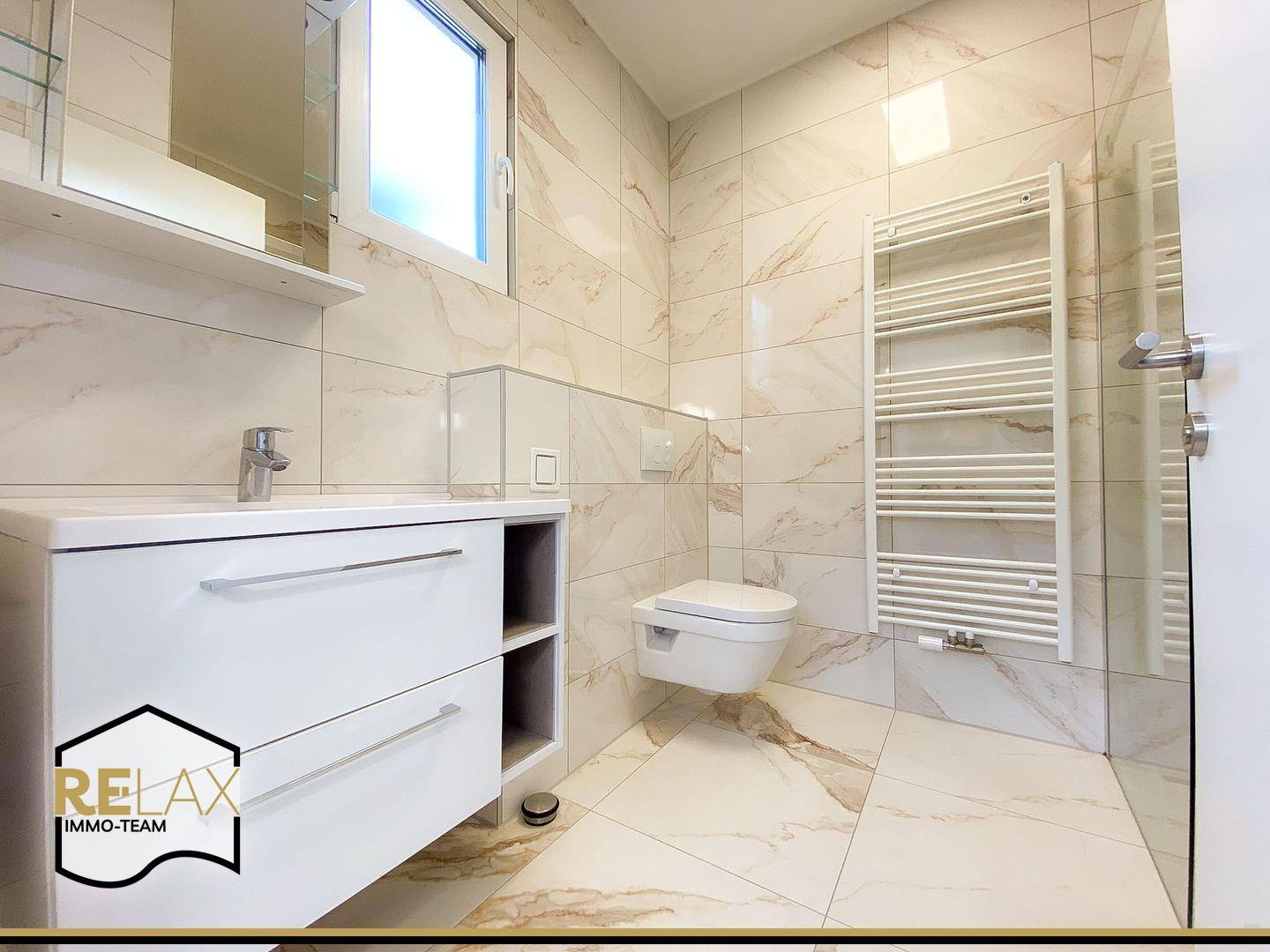 Elegantes Badezimmer mit Marmorfliesen, Waschtisch, Wand-WC und Fenster für Tageslicht.