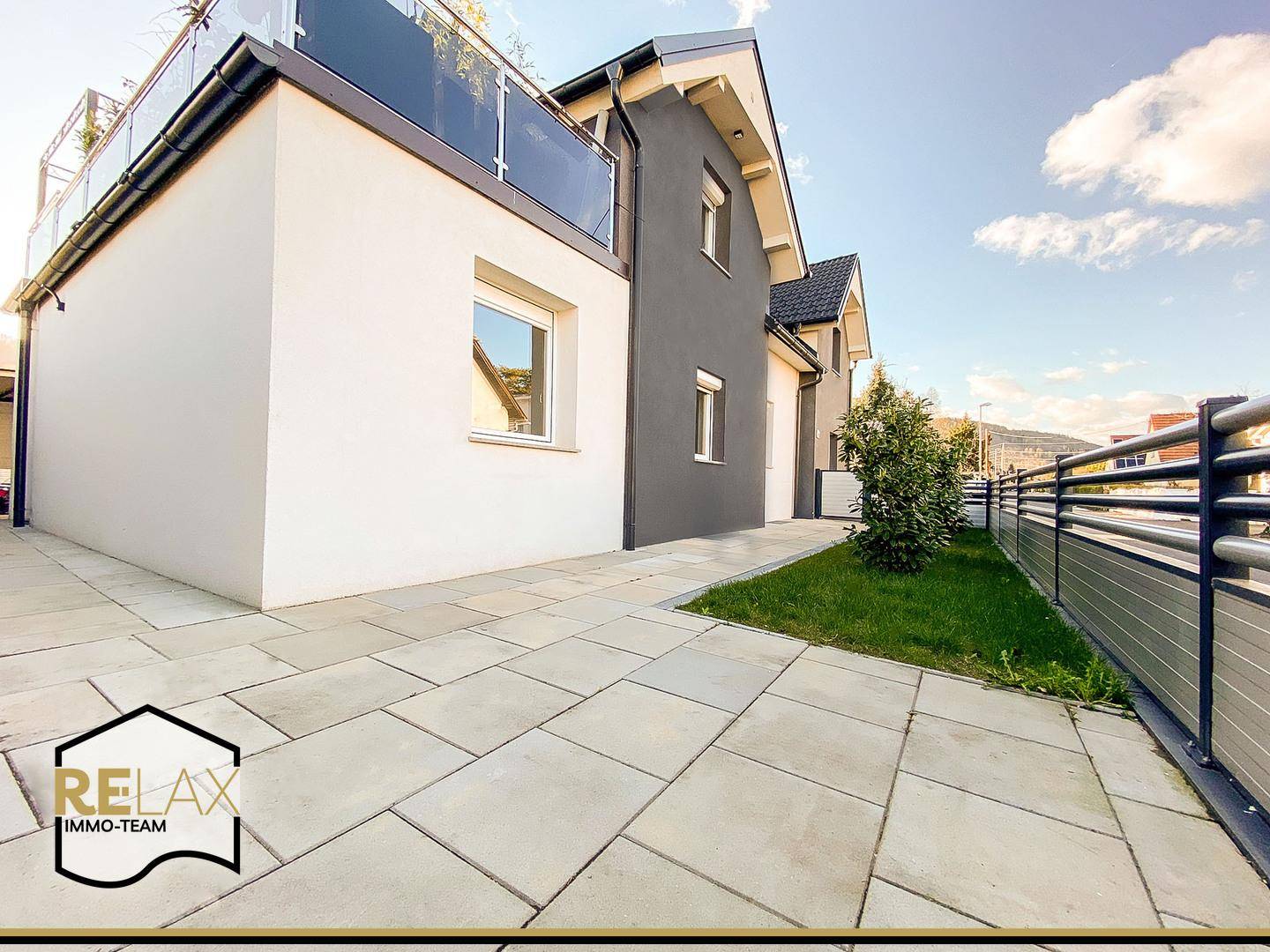 Gepflasterte Terrasse neben dem modernen Haus mit weißer und grauer Fassade, ideal für den Außenbereich.