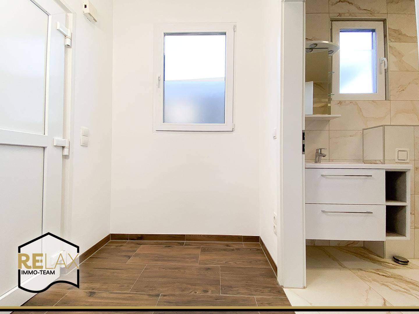 Eingangsbereich mit Fenster und Zugang zum Badezimmer, kombiniert mit dunklem Fliesenboden.