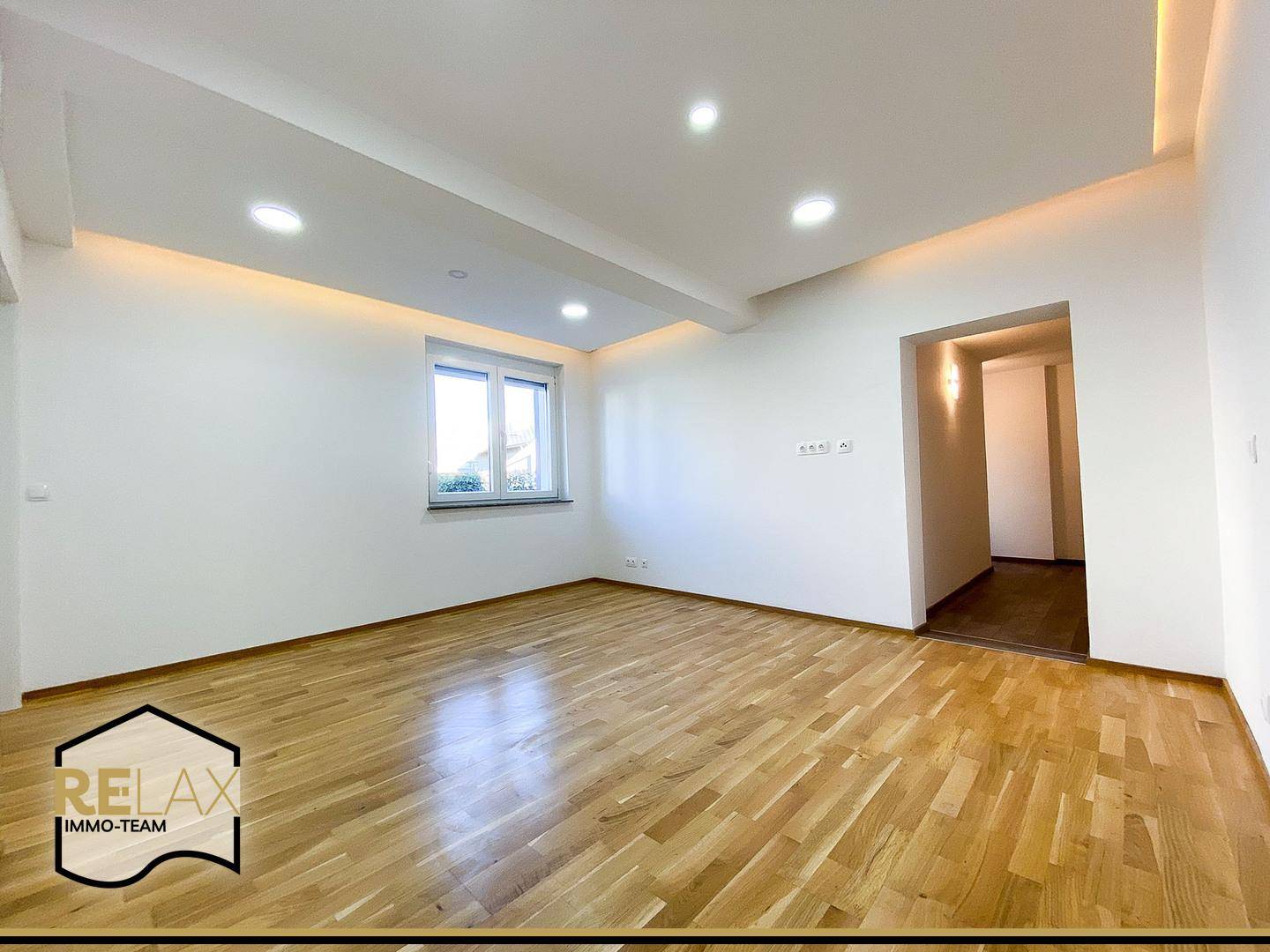 Geräumiges, leeres Zimmer mit hellem Parkettboden und integrierter Deckenbeleuchtung, ideal für Wohnzwecke.