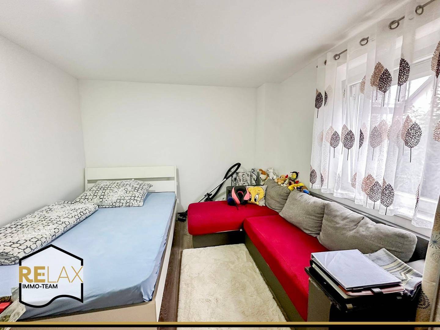 Gemütliches Schlafzimmer mit Einzelbett und Sofa, hell durch Fenster mit Vorhängen.