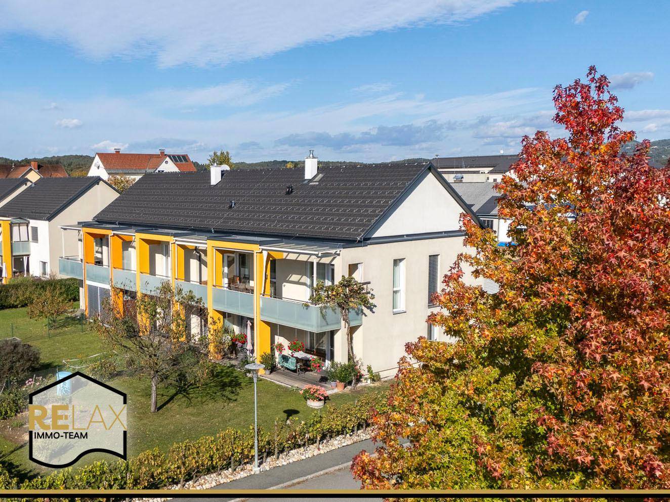 Ansicht der Wohnanlage mit herbstlicher Bepflanzung und klarem Himmel.