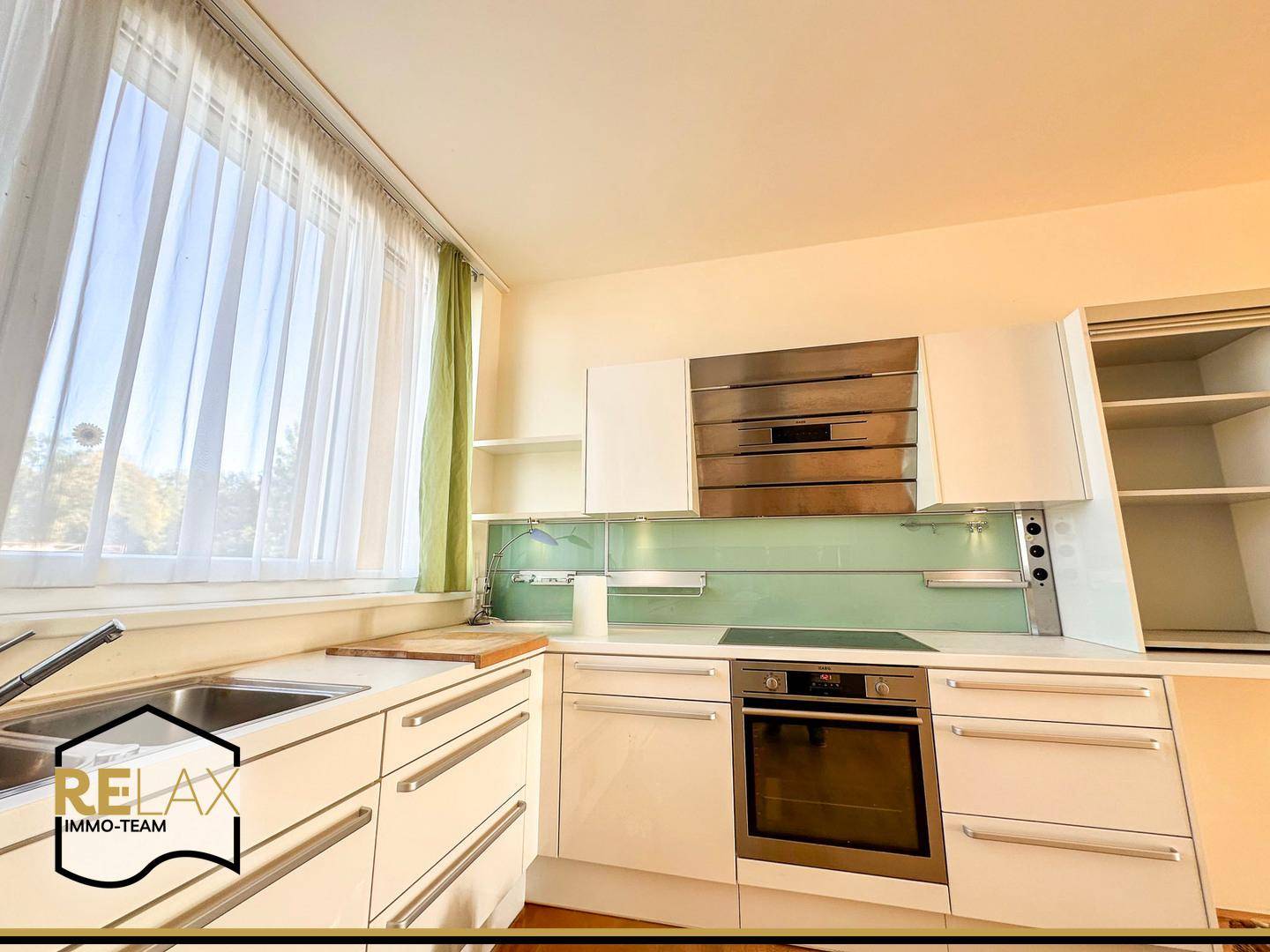 Moderne Einbauküche mit weißen Schränken, integrierten Geräten und grüner Rückwand.