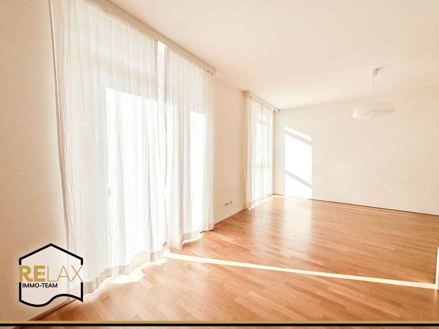 Lichtdurchflutetes Wohnzimmer mit hellem Holzboden und großen Fenstern für viel Tageslicht.