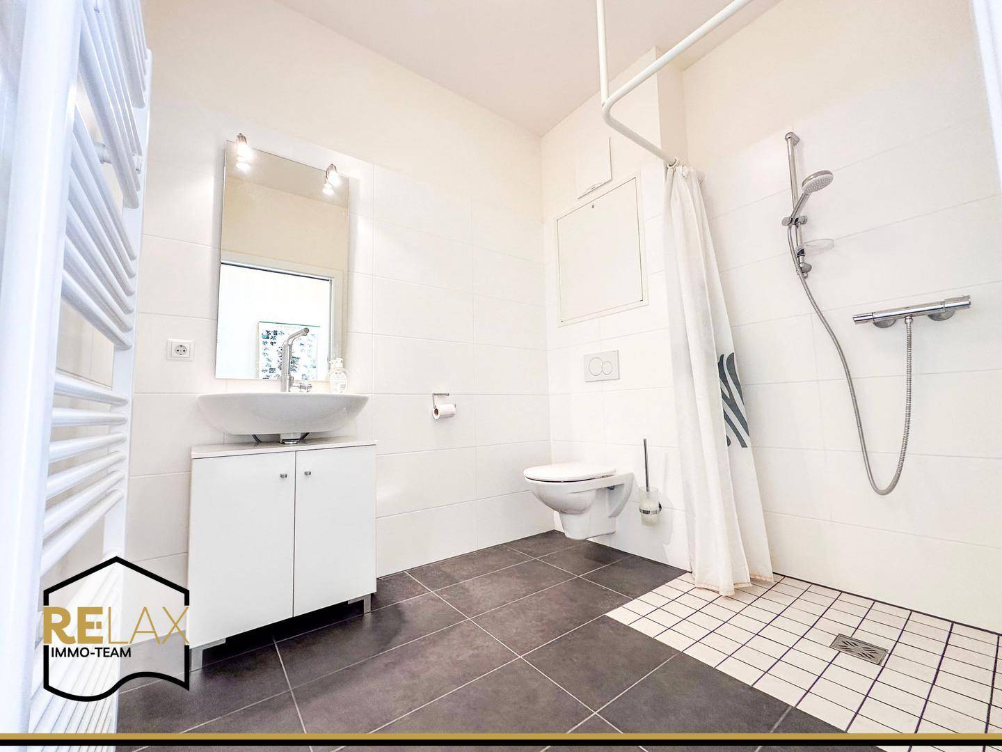 Modernes Badezimmer mit dunklen Fliesen, wandhängendem WC und ebenerdiger Dusche.