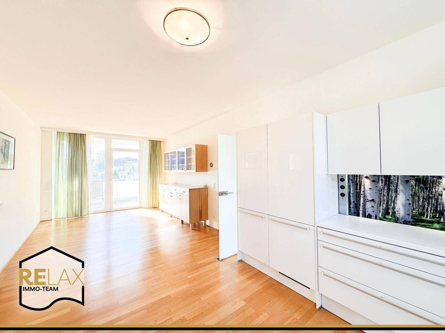 Offener Wohnbereich mit integrierter Küche, hellem Holzboden und Zugang zum Balkon.