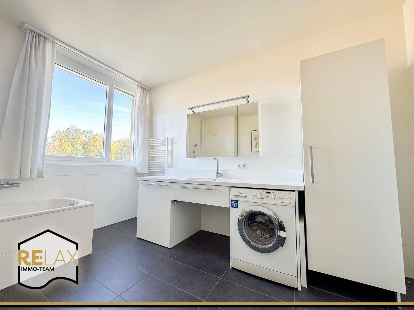 Geräumiges Badezimmer mit Badewanne, Waschmaschine und großem Fenster für Tageslicht.