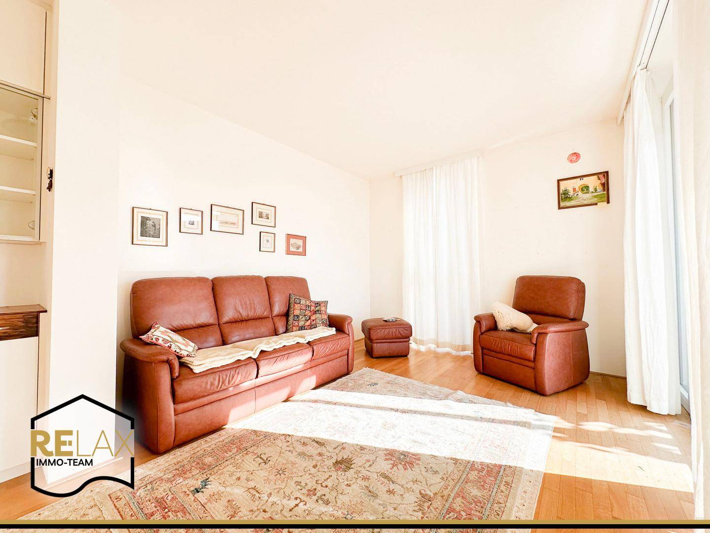 Gemütliches Wohnzimmer mit Ledersofa, Teppich und hellem Holzboden.