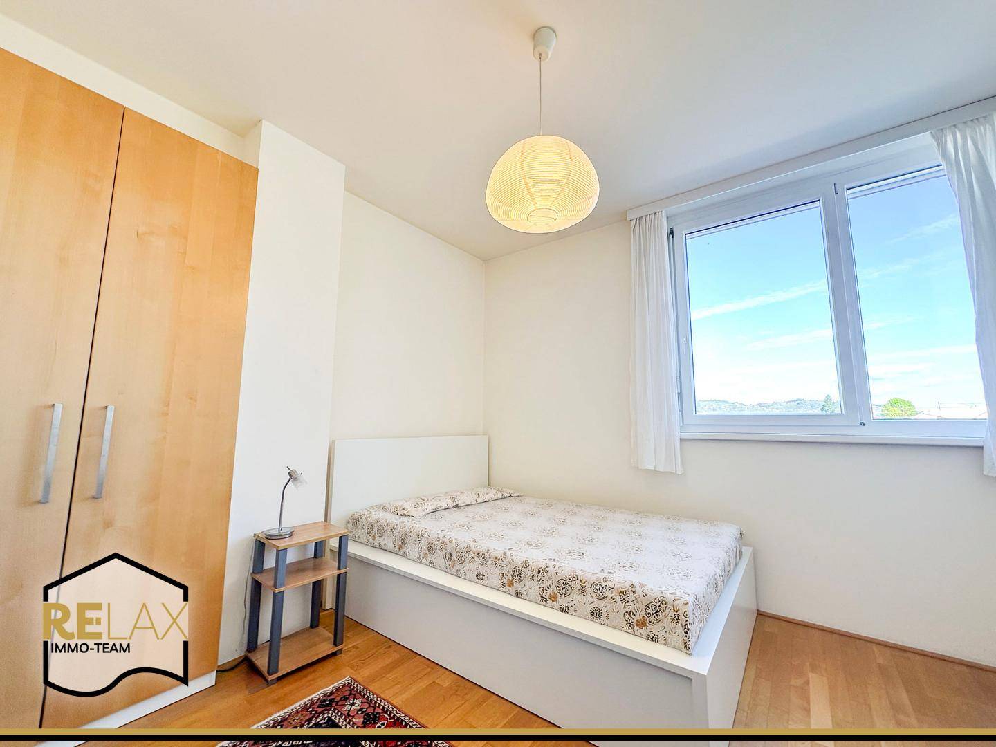 Helles Schlafzimmer mit Holzboden, großem Fenster und Blick ins Grüne.