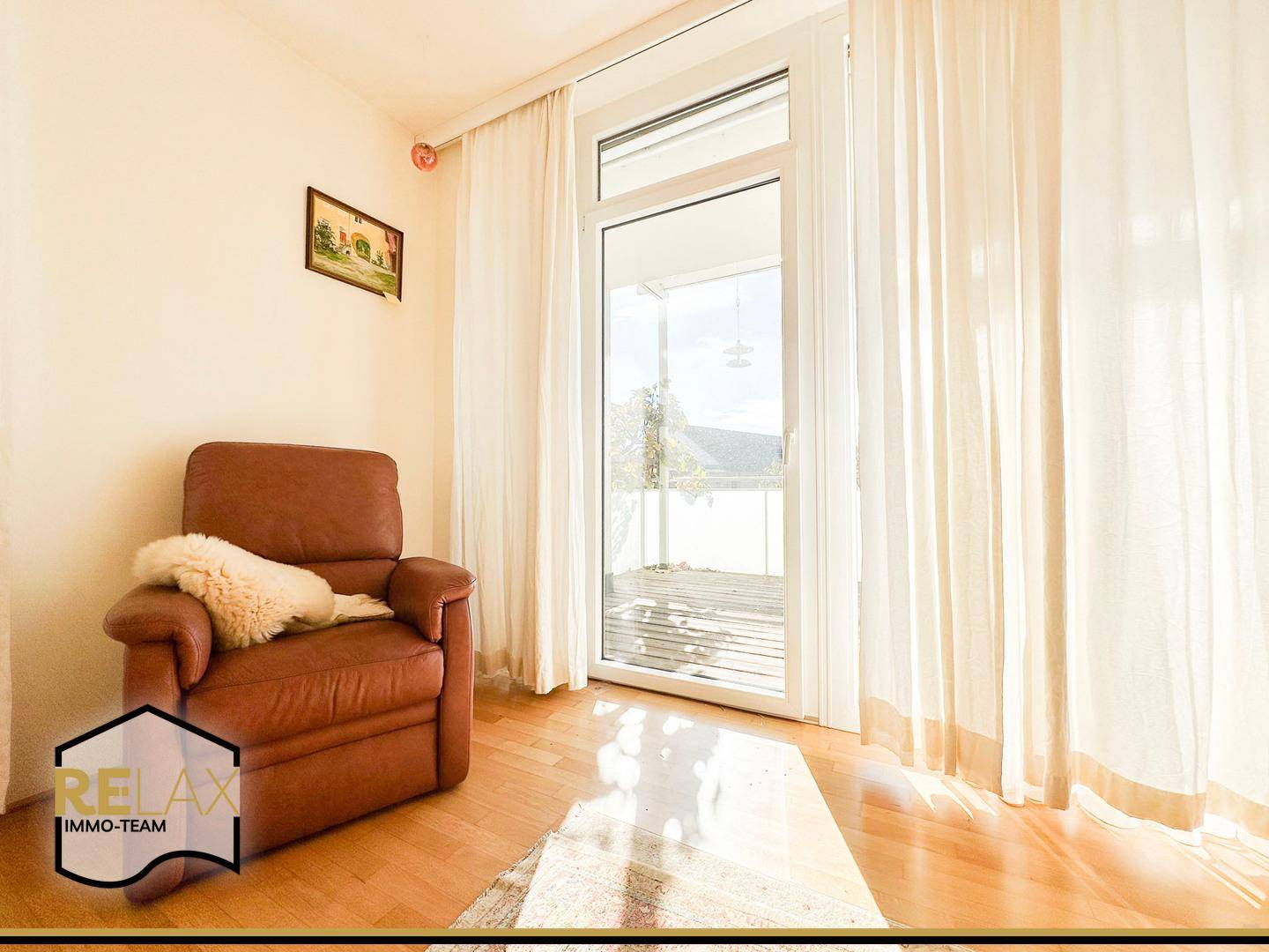 Heller Wohnbereich mit Ledersessel und Zugang zum sonnigen Balkon.