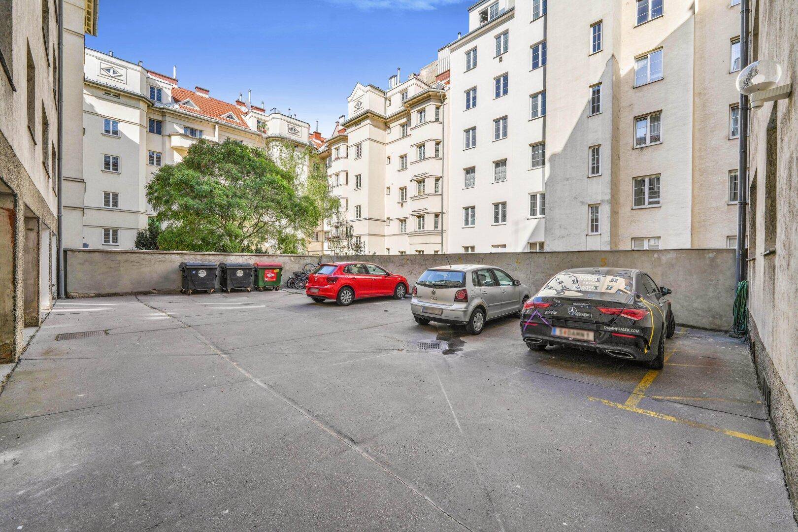 Offener Parkplatz im Innenhof, umgeben von Wohngebäuden, mit mehreren geparkten Autos.