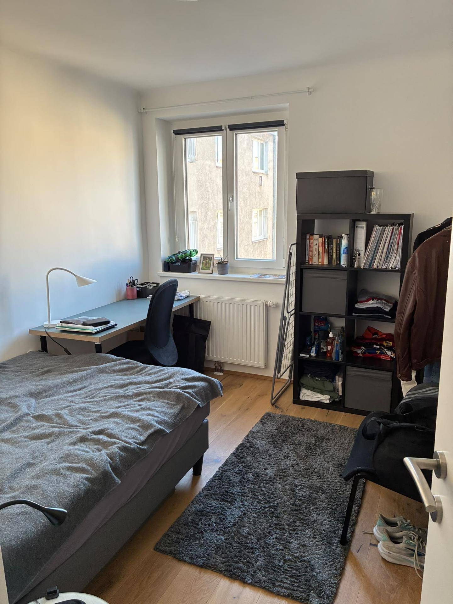 Helles Schlafzimmer mit Holzboden, einem Bett, Schreibtisch und einem Regal am Fenster.