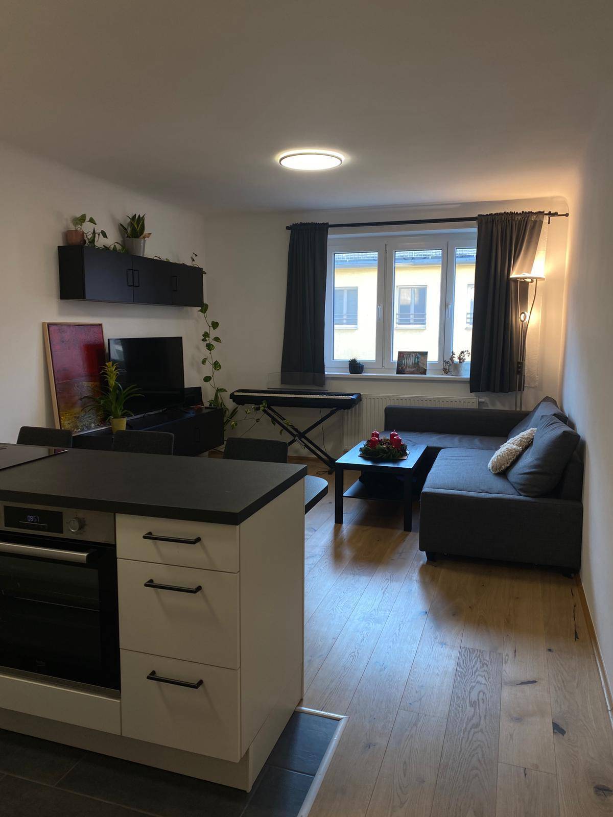 Heller Wohnbereich mit Sofa, Couchtisch und Blick auf die offene Küche, ausgestattet mit Holzboden.