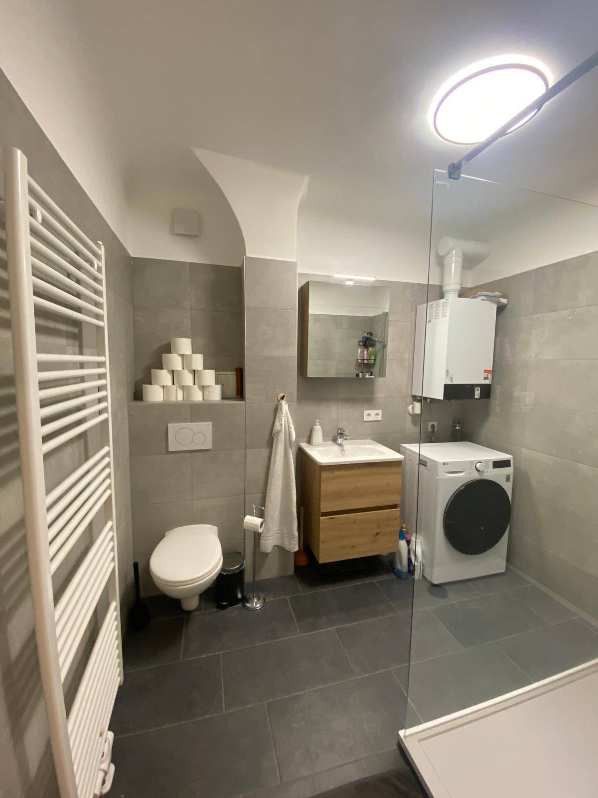 Badezimmer mit WC, Waschbecken, beheiztem Handtuchhalter und Waschmaschine, alles in modernem Design.